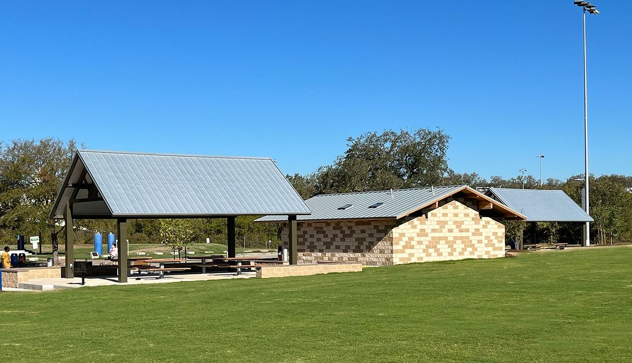 A couple of buildings in a grassy field with a blue sky in the background