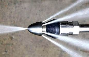 Close-up of a metal nozzle spraying several streams of water on a concrete surface