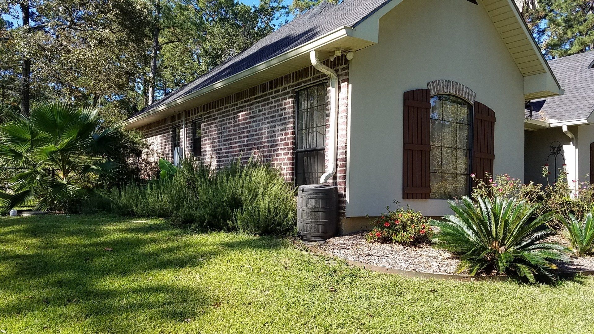 A white brick house with brown shutters is sitting on top of a lush green lawn.