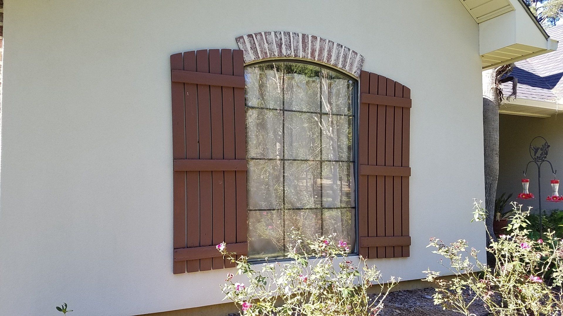 A white house with a window with brown shutters on it.