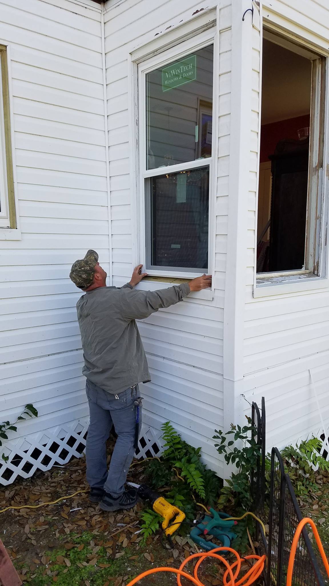A man is installing a window on the side of a white house.