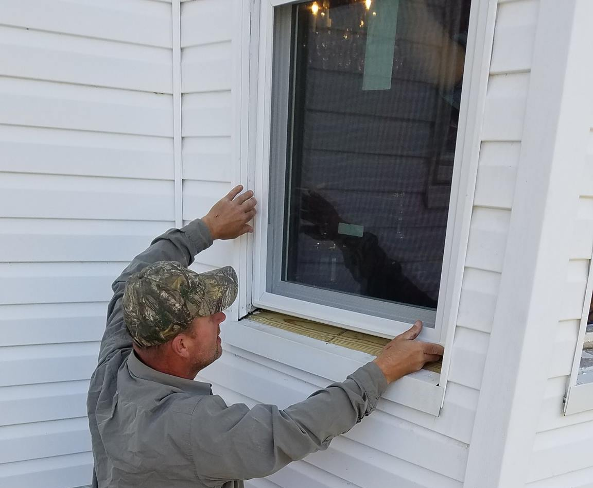 A man is installing a window on the side of a house.