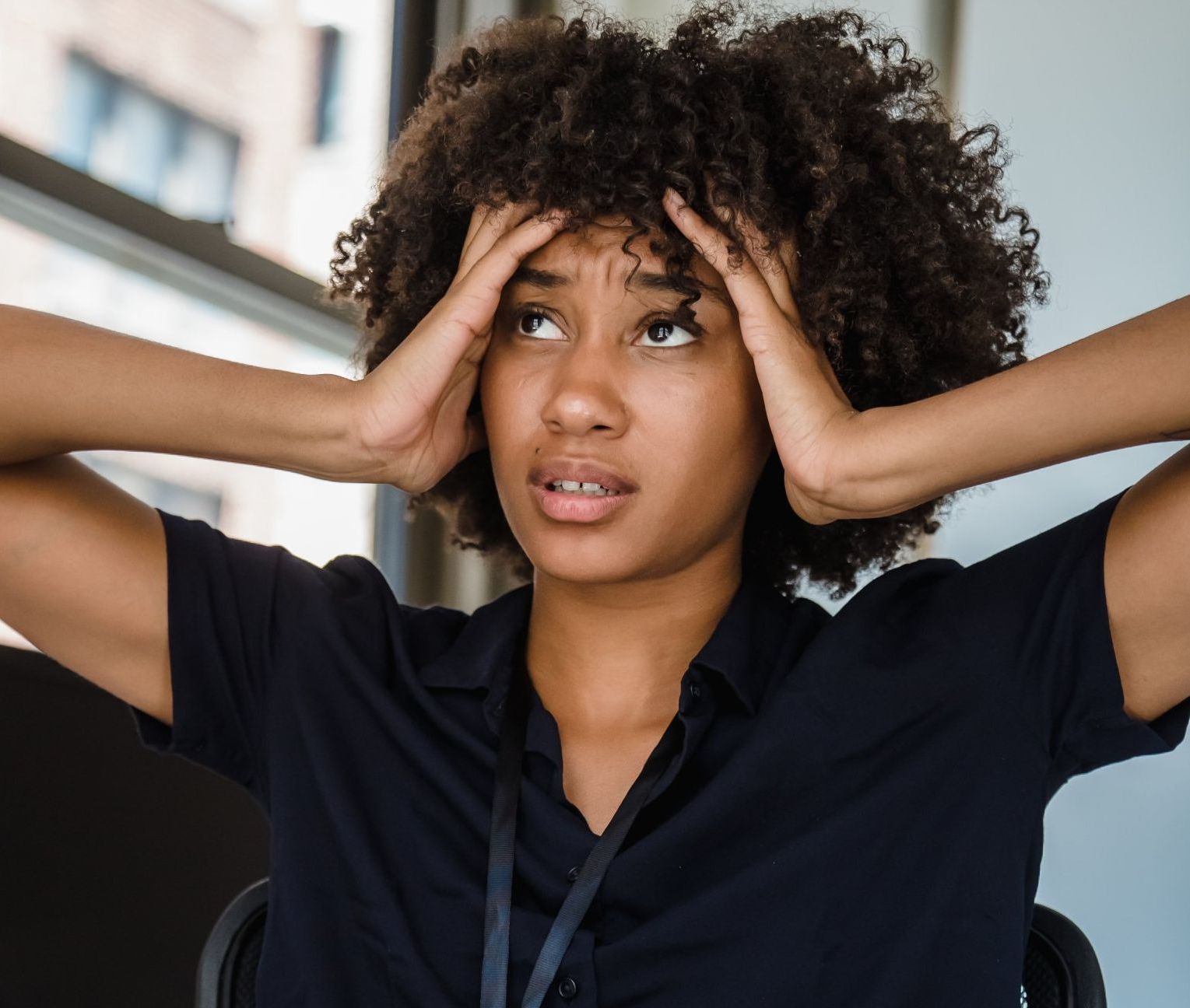 A woman with curly hair is sitting in a chair with her hands on her head.