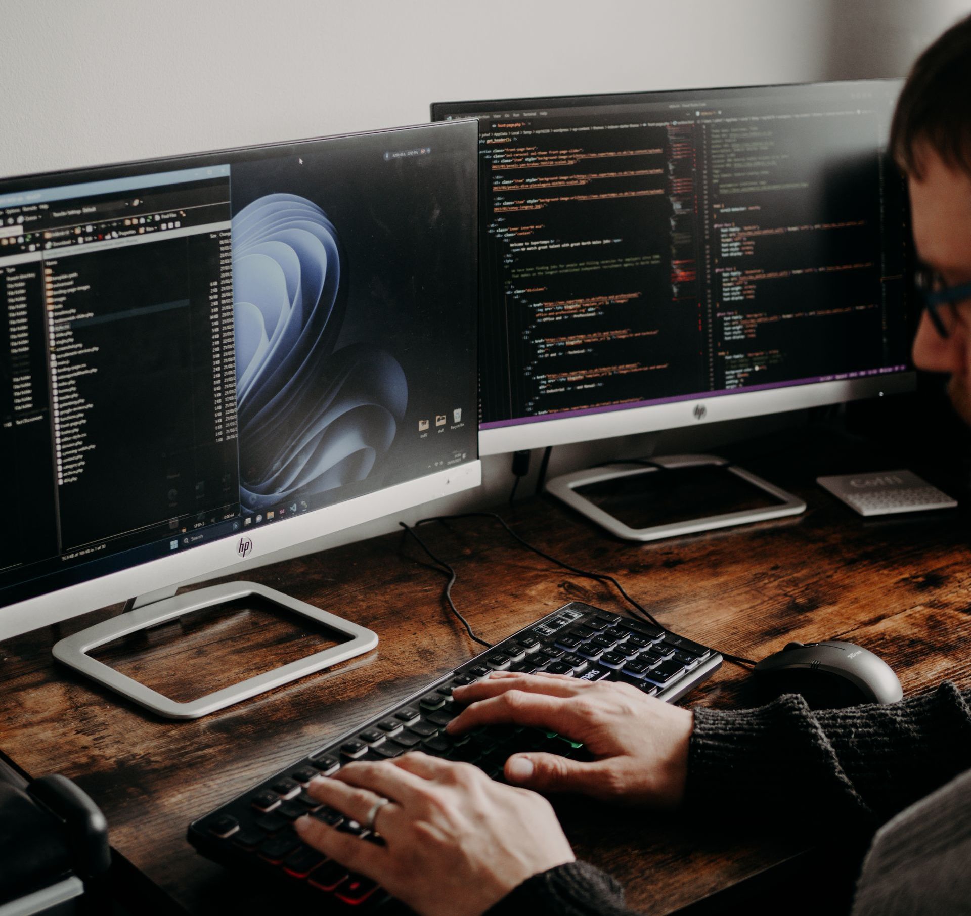 A man is typing on a keyboard in front of two computer monitors