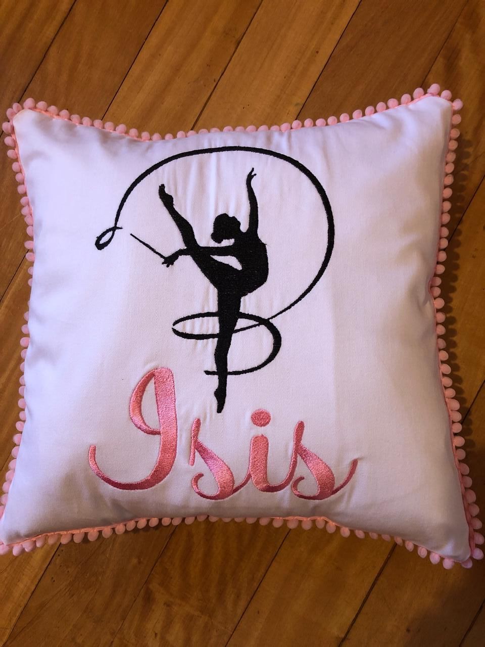 Almohada blanca con arcoíris bordado y nombre “Alma” en dorado; borde rosa.