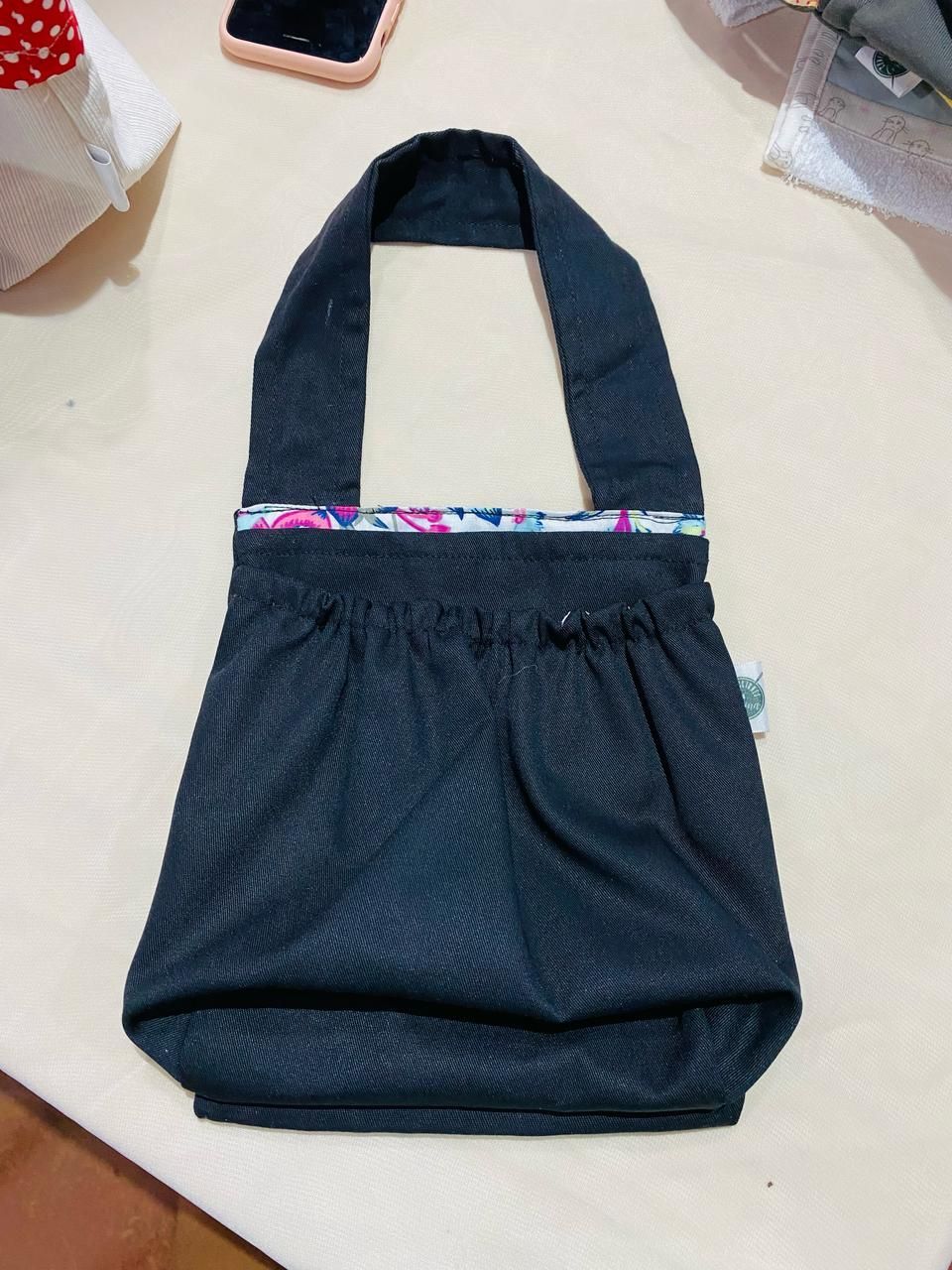 Bolso de mano de tela gris con diseño floral bordado en rojo y asa gris.