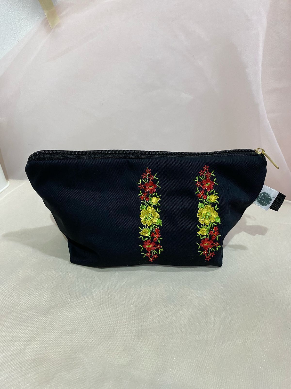 Bolsa de cosméticos de color beige con diseño de copo de nieve bordado en rojo.