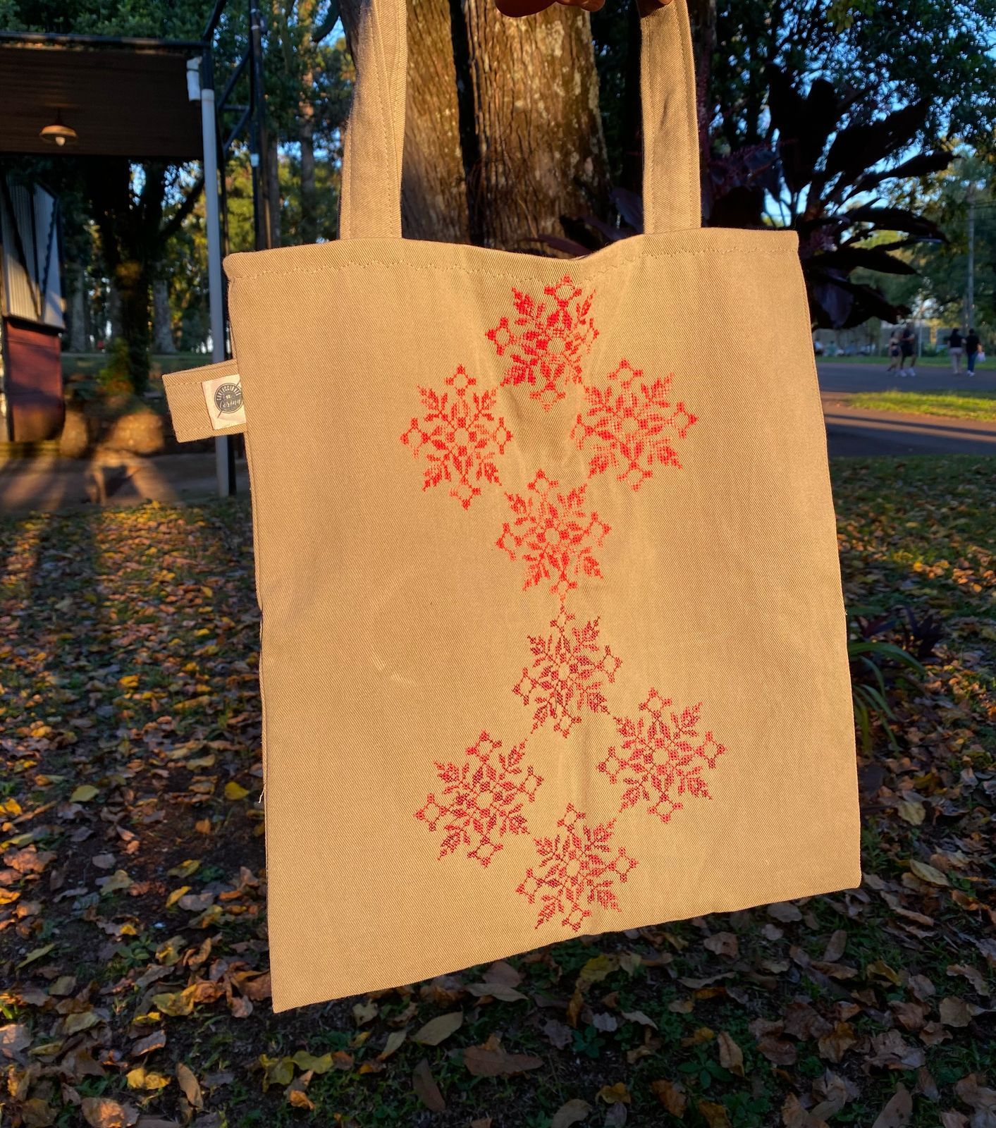 Bolso tote color canela con diseño geométrico bordado, colgado en un árbol.