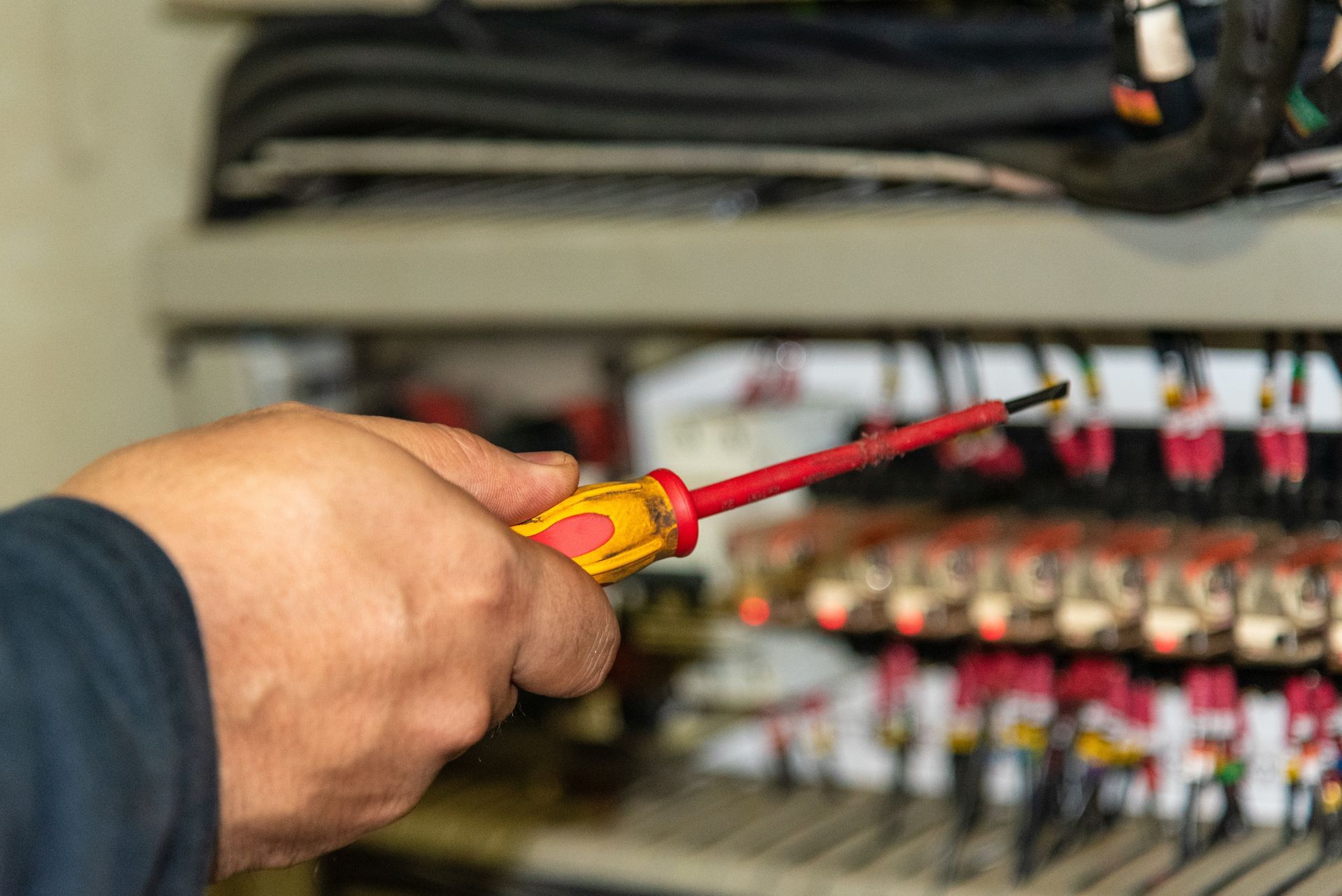 Hand using a red-and-yellow screwdriver to adjust electrical wiring in a control panel