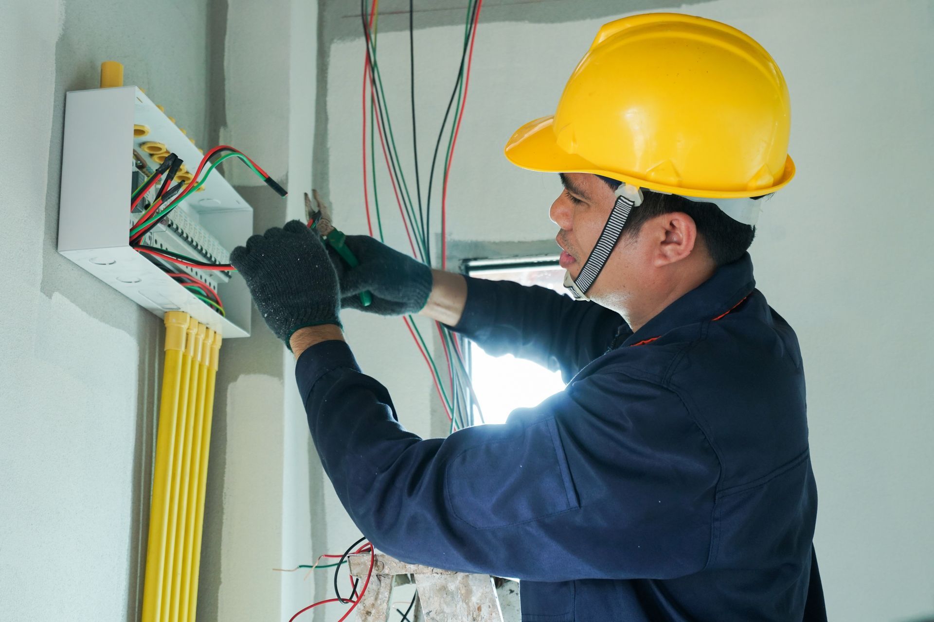 Electrician wearing a yellow hard hat wiring an electrical panel in a wall mount box