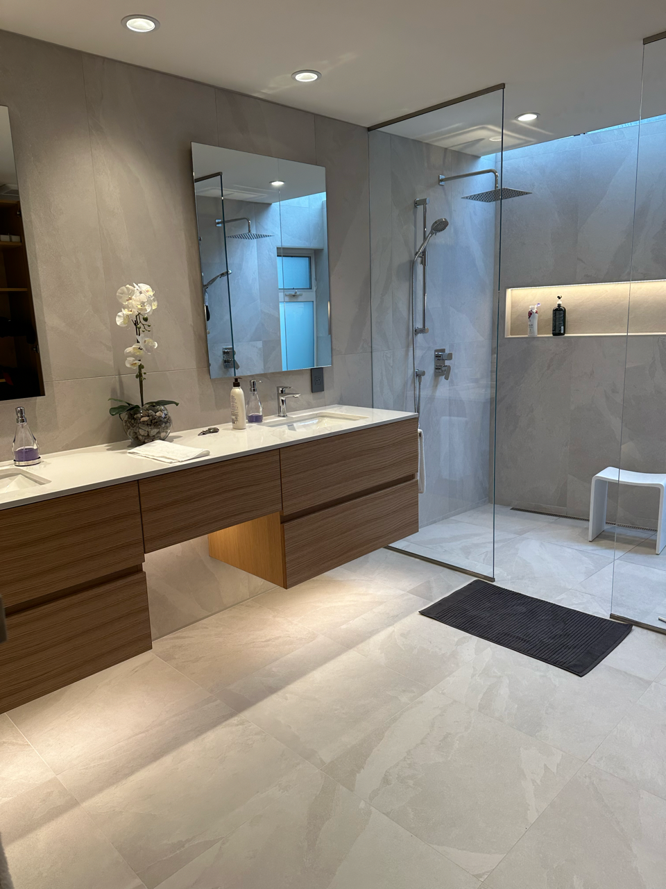 A bathroom with two sinks , a mirror and a walk in shower.