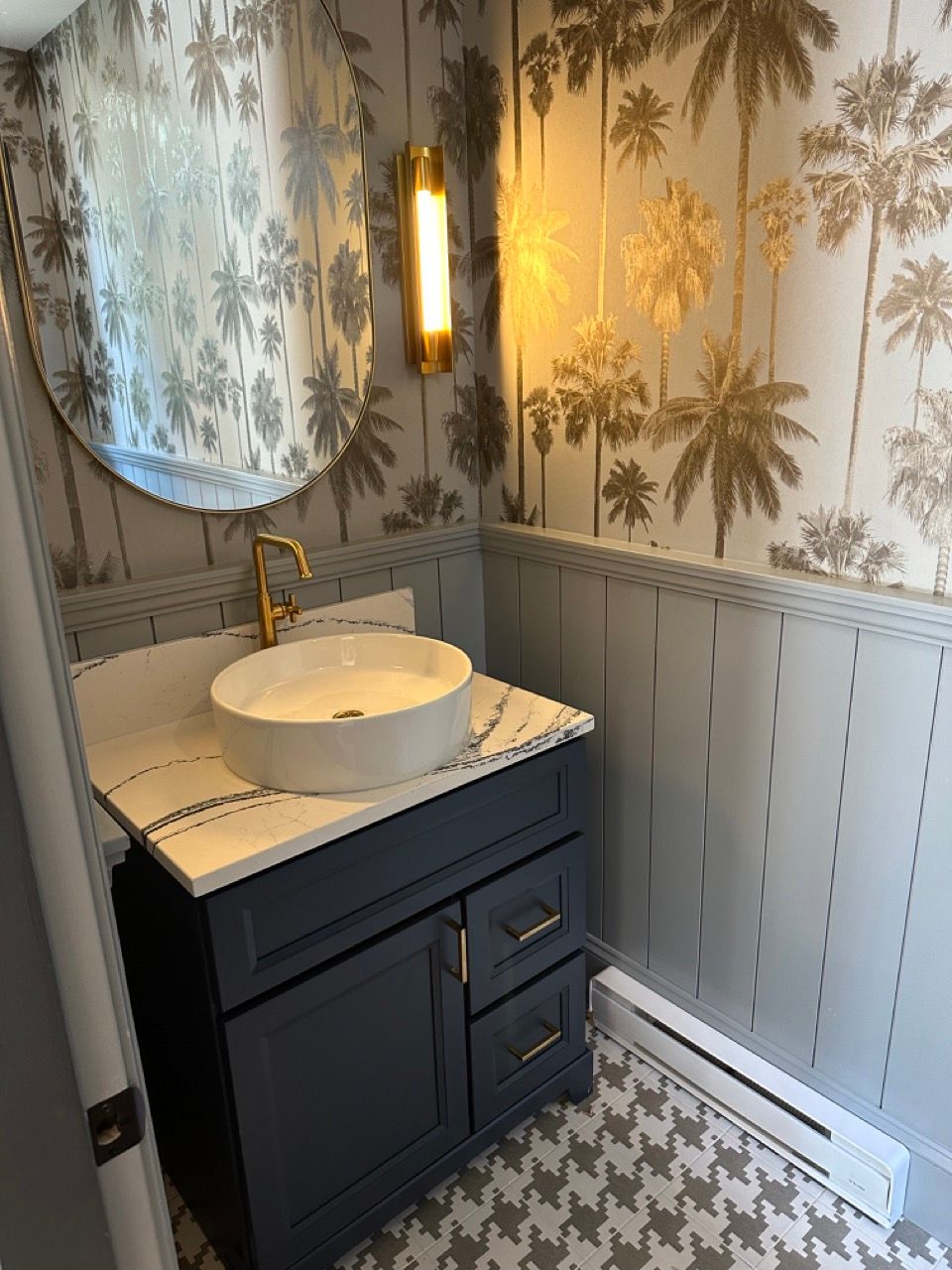 A bathroom with a sink , mirror , and palm trees on the wall.