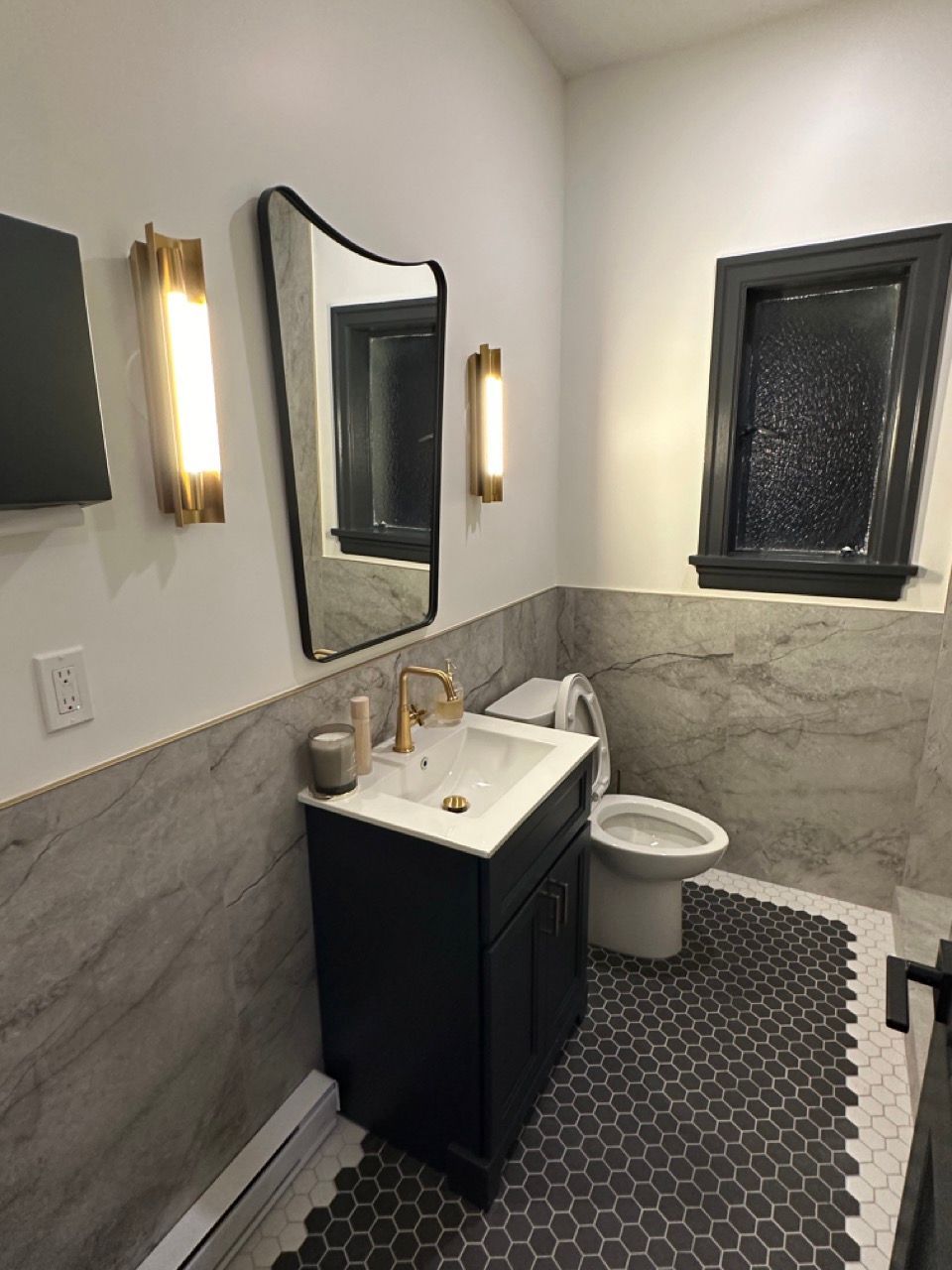A bathroom with a sink , toilet , mirror and window.