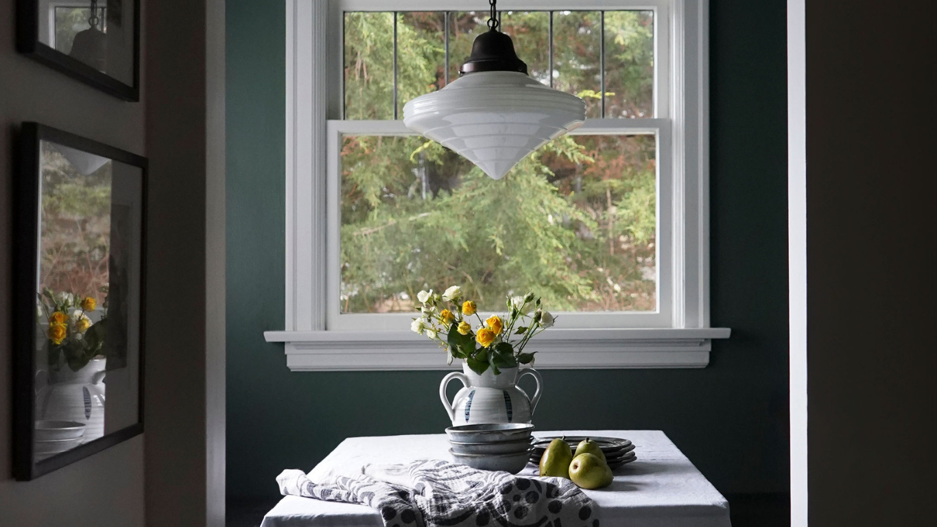 There is a table with a vase of flowers on it in front of a window.