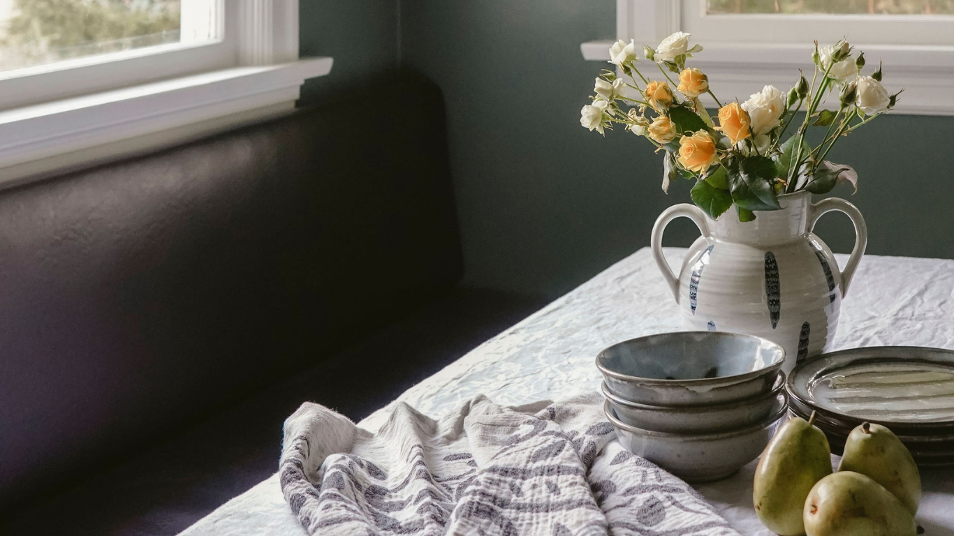 A table with bowls , plates , and a vase of flowers on it.