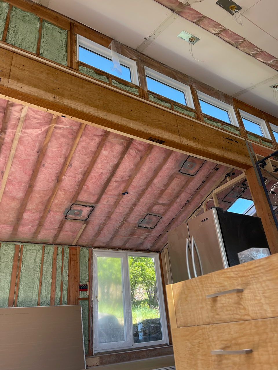 A kitchen under construction with pink insulation on the ceiling.