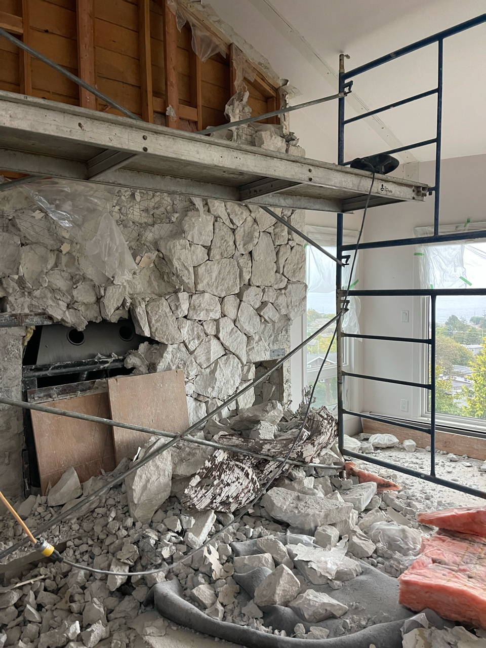 A stone fireplace is being demolished in a room with scaffolding.
