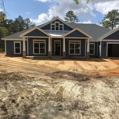 A newly constructed blue house with white trim, a covered porch, and a dirt yard with tire tracks.