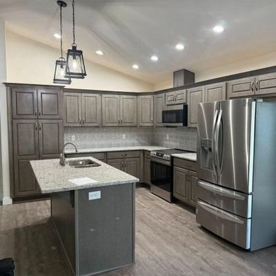 A modern kitchen with grey cabinets, granite countertops, a central island, and stainless steel appliances.