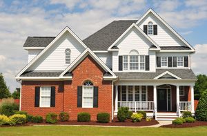 A two-story house with red brick and white siding, featuring a gray shingled roof, black shutters, and a front porch.