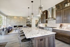 Modern open-concept kitchen with a granite island, dark wood cabinets, and a living area with a stone fireplace.