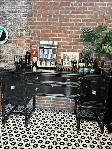 Black distressed buffet with items on top, set against a brick wall. Tiled floor.
