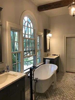 Elegant bathroom with arched window, freestanding tub, dark vanity, and patterned floor.