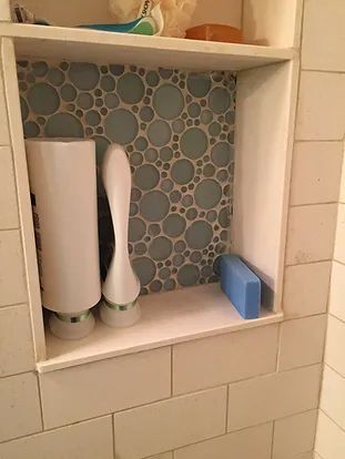 Bathroom niche with blue bubble tile background, holding white beauty tools and a blue sponge.