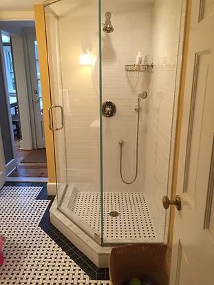 Glass shower with white tile walls and a black and white patterned floor in a bathroom.