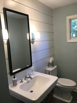 Bathroom with wall-mounted sink, toilet, and large mirror. Shiplap wall detail and blue-green walls.