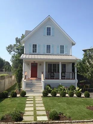 Light blue two-story house with red door, blue shutters, and a white porch; pathway leads to the entrance.