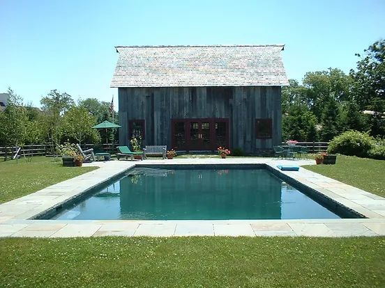 Backyard with pool, weathered barn, blue water, green grass, and sunny day.