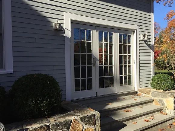 Exterior of a building with double doors, gray siding, stone steps, and landscaping.