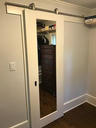 White mirrored sliding closet door, stainless steel track. Inside, a dresser and clothes are visible.