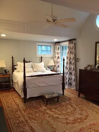 Bedroom with four-poster bed, patterned rug, white bedding, nightstands, and window with patterned curtains.