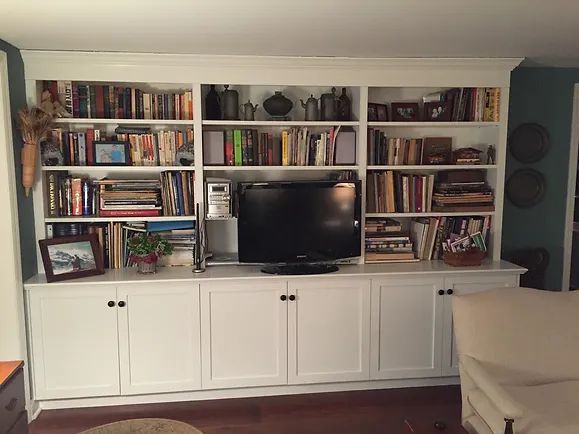 White built-in bookcase with books, TV, and cabinet doors. Set in a room with wood flooring.