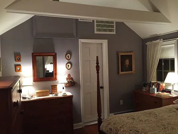 Bedroom with gray walls, wood furniture, and a white door; a mirror and artwork adorn the walls.