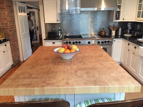 Kitchen with wooden island, stainless steel backsplash, white cabinets, and bowl of fruit.