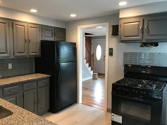 Kitchen with gray cabinets, black appliances, granite counters, and a doorway to stairs.