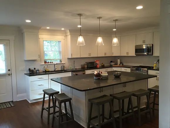 A modern kitchen with white cabinets, dark countertops, and a gray island with bar stools.