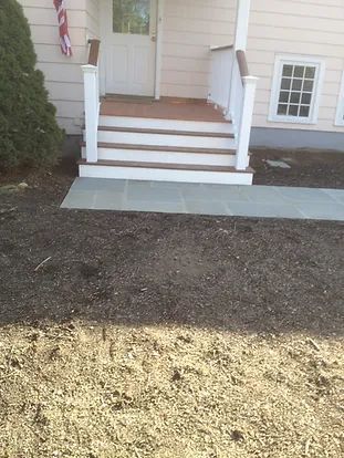 A light pink house with white porch and steps, a gray stone walkway, and dirt in front.