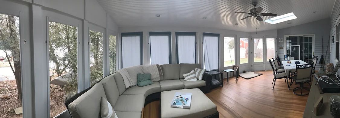 A bright, sun-filled room with wrap-around windows, a sectional sofa, and a dining table.