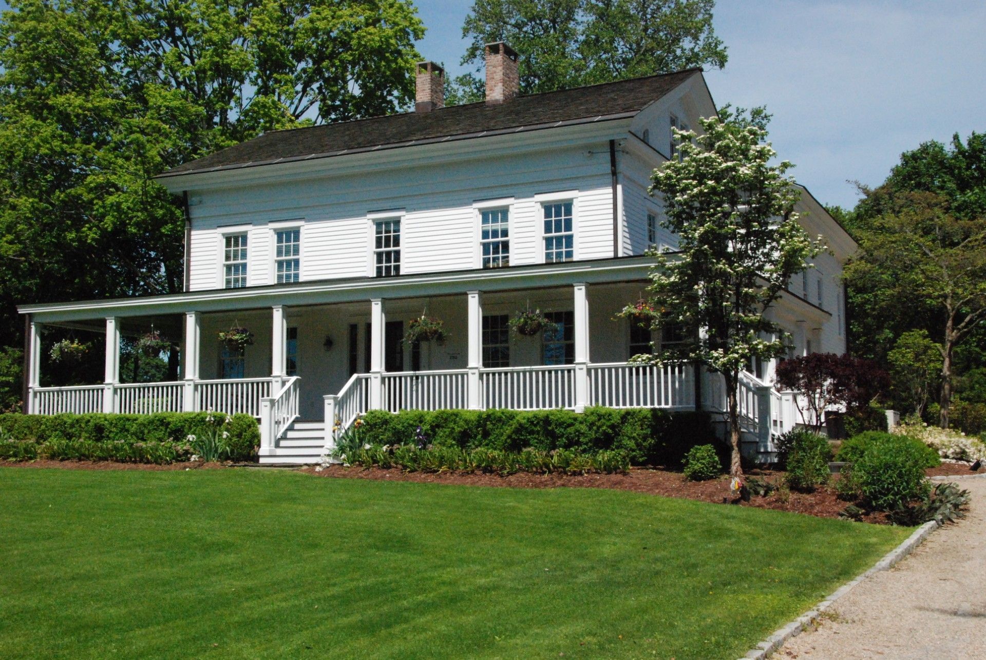 White two-story house with a porch and green lawn, surrounded by trees.