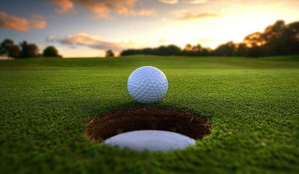 Golf ball perched on the edge of the hole on a green golf course at sunset.