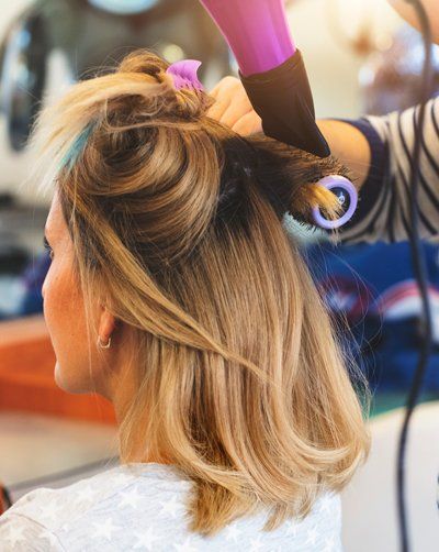 Female hairdresser using hairbrush and hair dryer