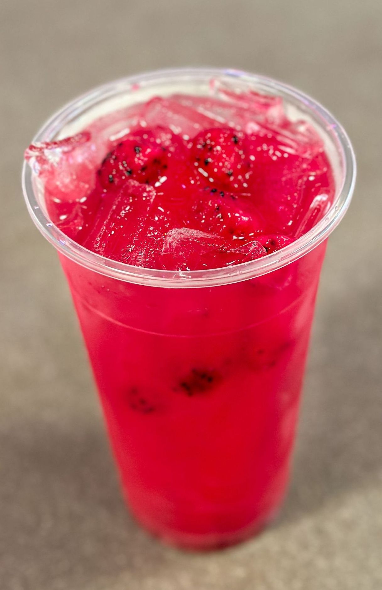 A close up of a red drink in a plastic cup on a table.