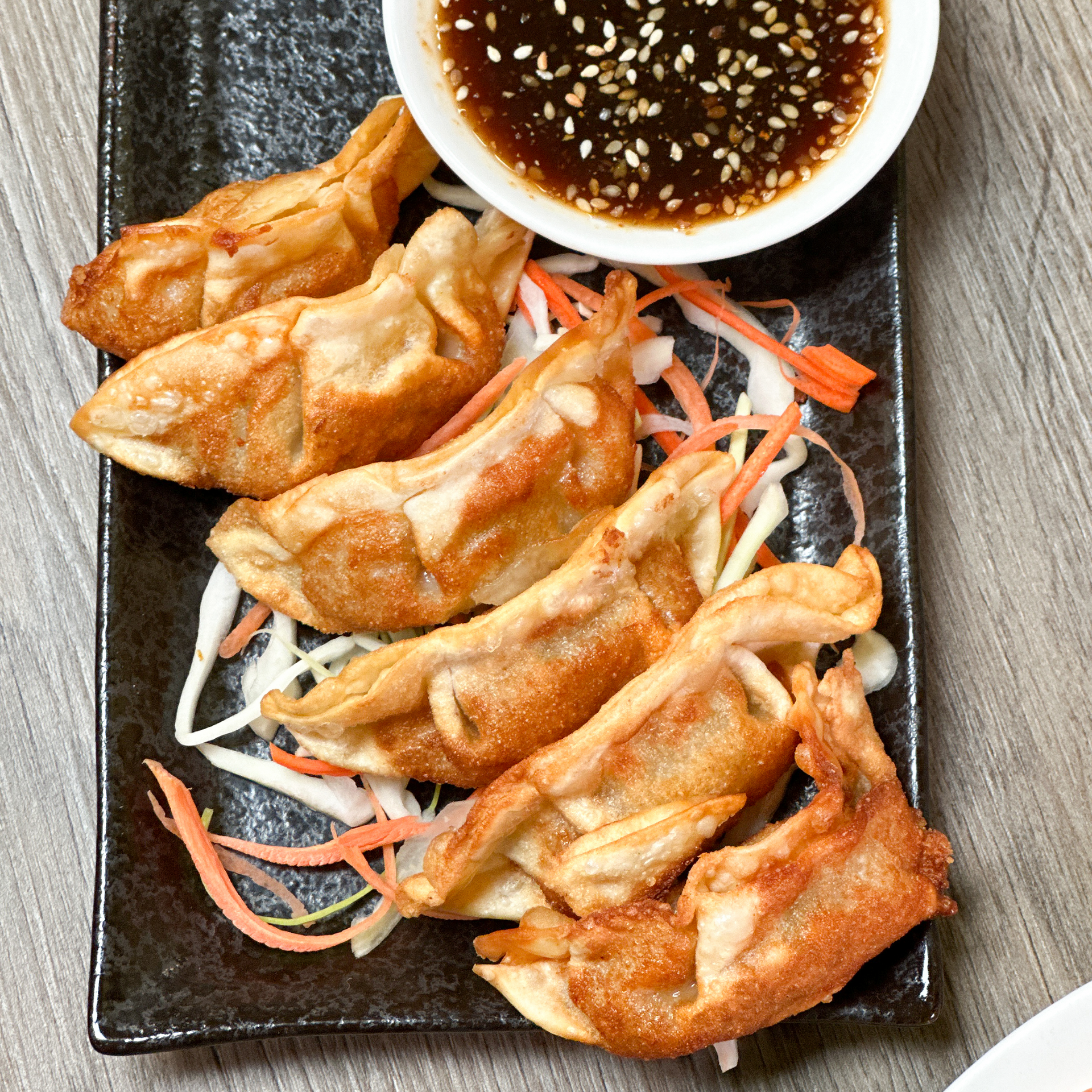 A black plate topped with fried dumplings and a bowl of dipping sauce