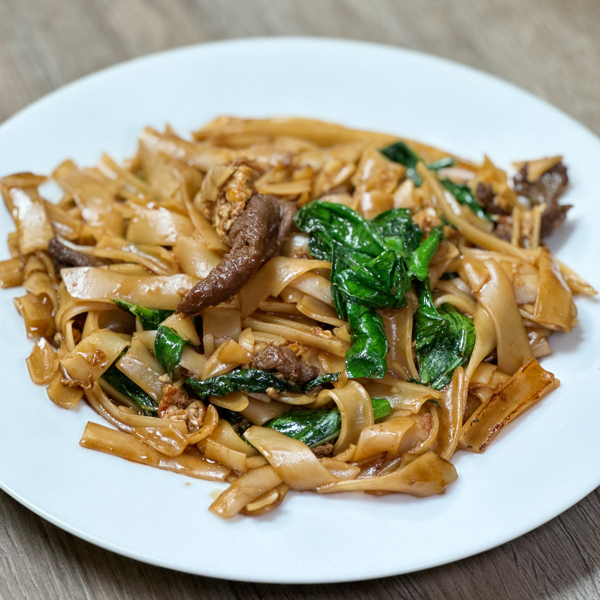 A white plate topped with noodles and meat on a wooden table.