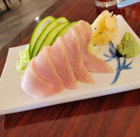 A white plate topped with sliced fish and cucumber on a wooden table