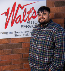 A man in a plaid shirt is standing in front of a walt 's auto service sign. | Walt's Auto Service